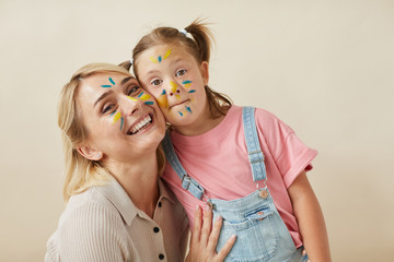 Portrait of happy mother and daughter with painted faces embracing each other and smiling at camera...