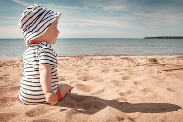 Little baby boy sitting on the beach in summer day