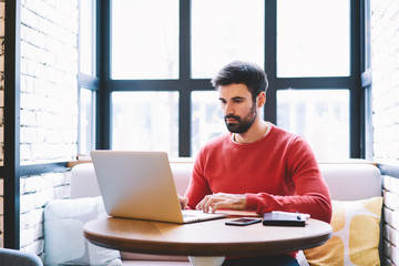 Pondering handsome skilled developer watching training webinar in web page on laptop connected to...