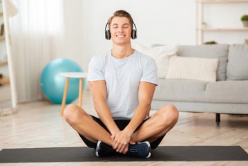 Music for training, yoga and relax. Happy young sportsman with closed eyes sits in lotus pose on mat