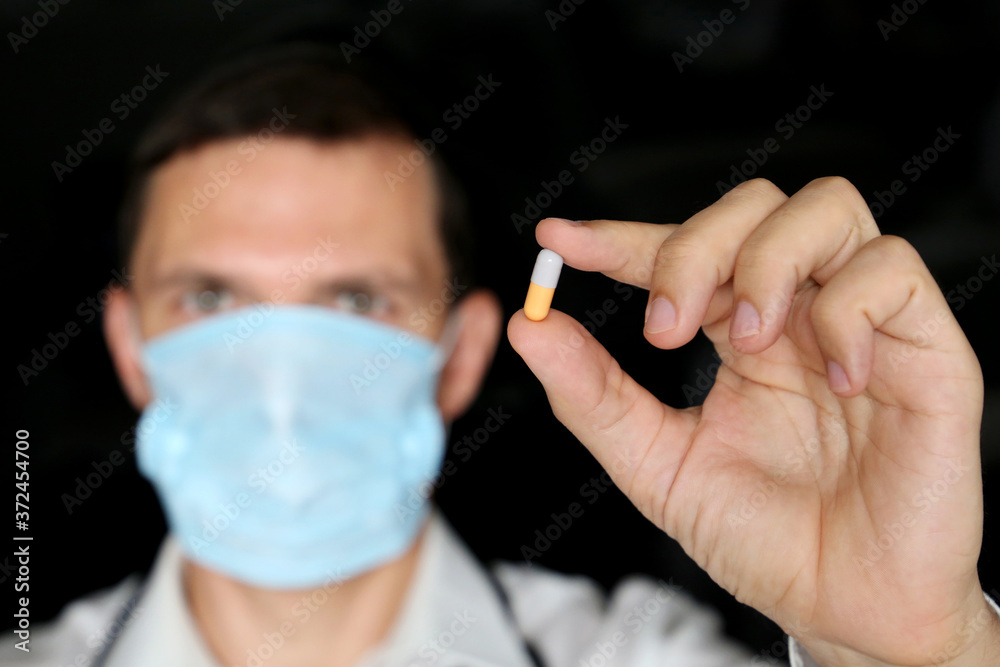 Wall mural doctor in medical mask holding pill, male hand with medication in capsule close up. concept of pharm