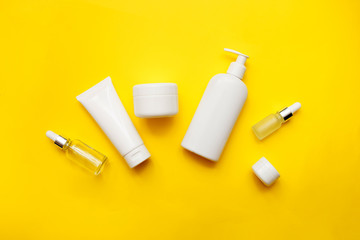 Cosmetics bottles on bright yellow background, top view, copy space. Mock up. White jars, bath accessories. Face and body care concept
