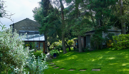 August and dappled sun lights a traditional Yorkshire Dales stone-built cottage and garden and garden shed