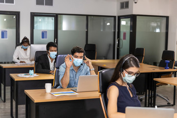 Business worker wearing face mask when working in the office to protect virus infection as part of business new normal. Workers keep social distancing to prevent COVID-19 infection