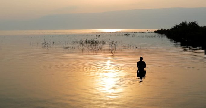 Man dipped in the water of Galilee Lake in Israel at sunrise.