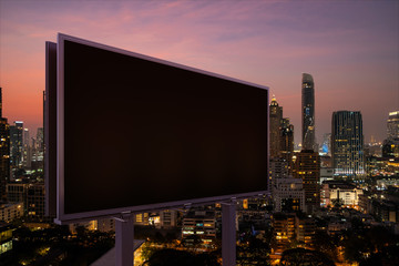 Blank black road billboard with Bangkok cityscape background at night time. Street advertising poster, mock up, 3D rendering. Side view. The concept of marketing communication to promote idea. © VideoFlow