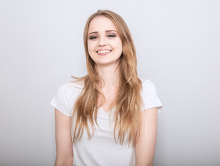 Pretty toothy laughing young woman with fair blond long hair in casual dress. Studio shot of good looking beautiful woman isolated against grey studio wall