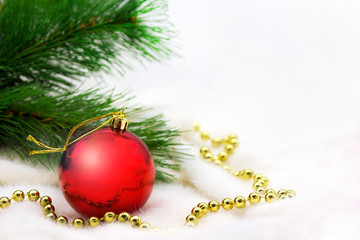 Red ornament ball on white christmas background next to green tree branches and gold decoration. space for text.New Year and Christmas mood concept.
