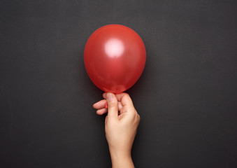 female hand holding an inflated red air balloon on a black background