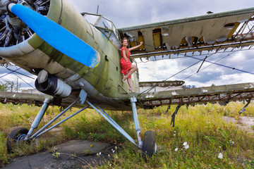 Attractive young woman stands on the wing of an abandoned green plane