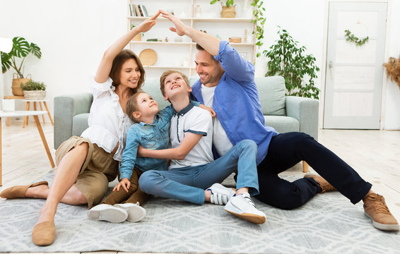 Young parents joining hands making roof sitting with children indoor