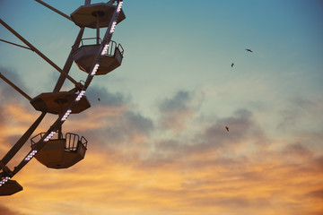 Ferris Wheel with sunset sky with clouds and flying birds