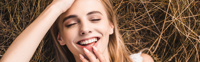 Obraz premium website header of excited young woman touching lips and forehead while lying on green grass, top view