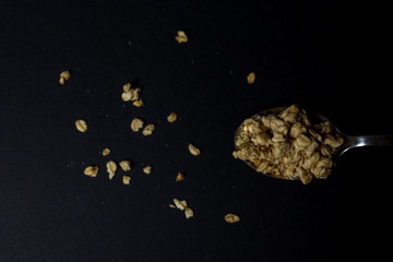 granola in a spoon on a black background.