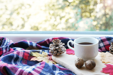 Cup of autumn coffee or chocolate and yellow dry leaves near a window, copy space