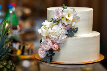 Tall sweet wedding cake decorated with live pink and white flowers on a table.