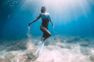 Fototapeta na wymiar Attractive woman freediver glides and posing with sandin hands over sandy bottom with white fins.