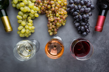 Glasses with white, red and pink wine and ripe grapes on black stone background, top view
