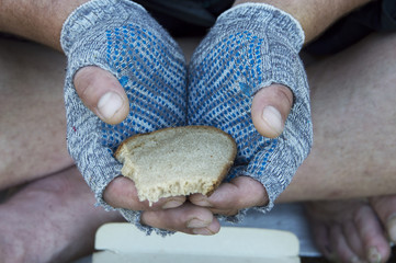 A piece of rye bread in the hands of a homeless man in gloves. Poverty, unemployment, hunger.