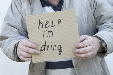 The hands of a homeless person hold a sign with the inscription. Poverty, unemployment.