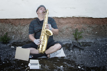 A homeless street musician sits on the street with a saxophone to earn food.