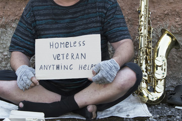A homeless street musician sits on the street with a saxophone to earn food.