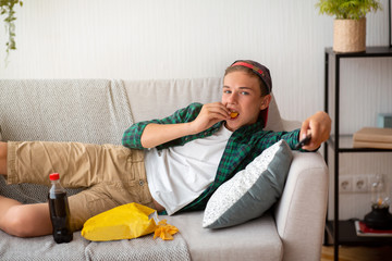 Teen guy eating chips and watching TV at home