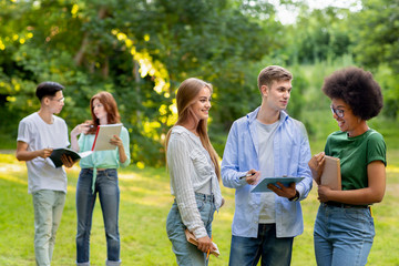 Multi ethnical teenage classmates resting outdoors between classes, chatting and smiling together