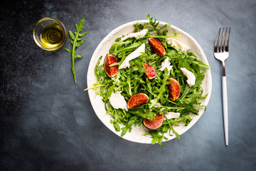 Delicious salad with figs, arugula and goat cheese on white plate, top view, copy space