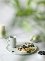 Concept of a minimalistic healthy breakfast made from yogurt, granola, blueberries, milk, tea and boiled eggs. Light background, copy space