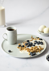 Concept of a minimalistic healthy breakfast made from yogurt, granola, blueberries, milk, tea and boiled eggs. Light background, copy space