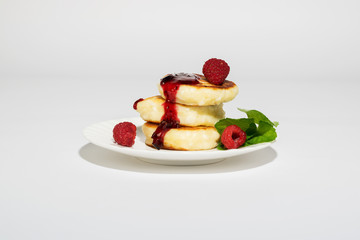 Delicious and healthy cottage cheese pancakes on a white saucer, poured with BlackBerry jam.