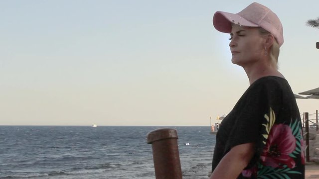 on a summer day, a beautiful young woman stands by the sea and looks at the waves. Dressed in a cap and sun cloak made of burnus. Enjoying a seaside vacation