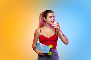 Skatergirl with coffee. Caucasian young woman's portrait on gradient studio background in neon. Beautiful female model in casual style. Concept of human emotions, facial expression, youth, sales, ad.