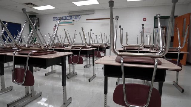 Slider shot to the right of empty school classroom with chairs on the desks.