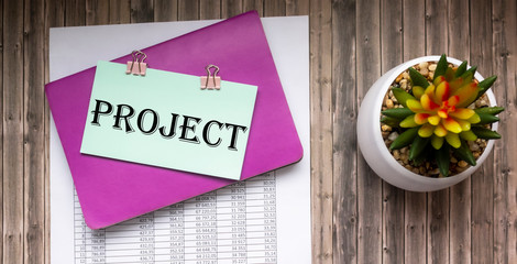 The draft text is written on a sticker. On a wooden table there is a cactus flower, a notebook and a document with numbers