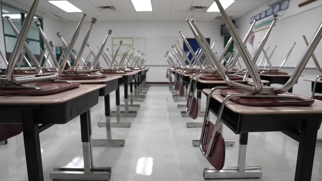 Slider shot to the left of empty school classroom with chairs on the desks.