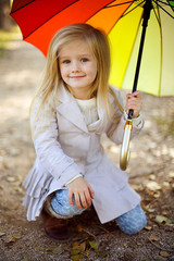 Cute little girle with umbrella in autumn park.