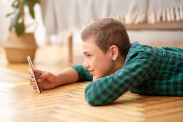 Happy teenager using mobile phone, laying on floor at home