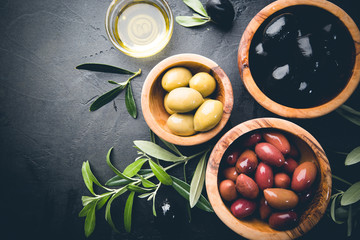 Black and green olives and olive oil in wooden bowls on black background. Top view with copy space for text.