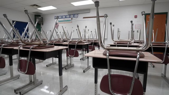 Slider shot to the left of empty school classroom with chairs on the desks.