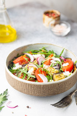 Eggplant salad with tomatoes, arugula and feta cheese in a bowl on white background
