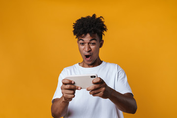 Image of excited african american guy playing online game on cellphone