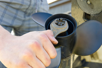 man changing propeller on outboard motor. Repairing outboard motor for boat, replacing screw.