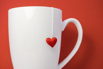 on a red background is a large white cup with a heart hanging on it
