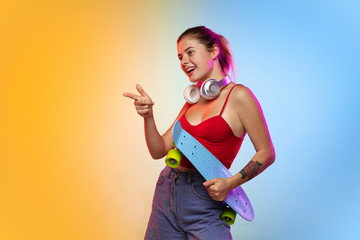 Pointing, showing. Caucasian young woman's portrait on gradient studio background in neon. Beautiful female model in casual style. Concept of human emotions, facial expression, youth, sales, ad.