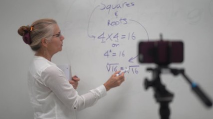 Focus shift of woman teaching math at white board in front of smartphone for virtual learning during pandemic.