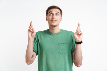 Image of young caucasian man in basic t-shirt praying and keeping fingers crossed