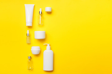 Cosmetics bottles on bright yellow background, top view, copy space. Mock up. White jars, bath accessories. Face and body care concept