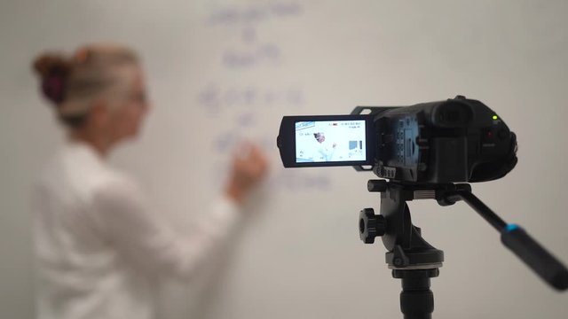 Focus shift from camera to teacher giving a virtual math class online to students during a pandemic.
